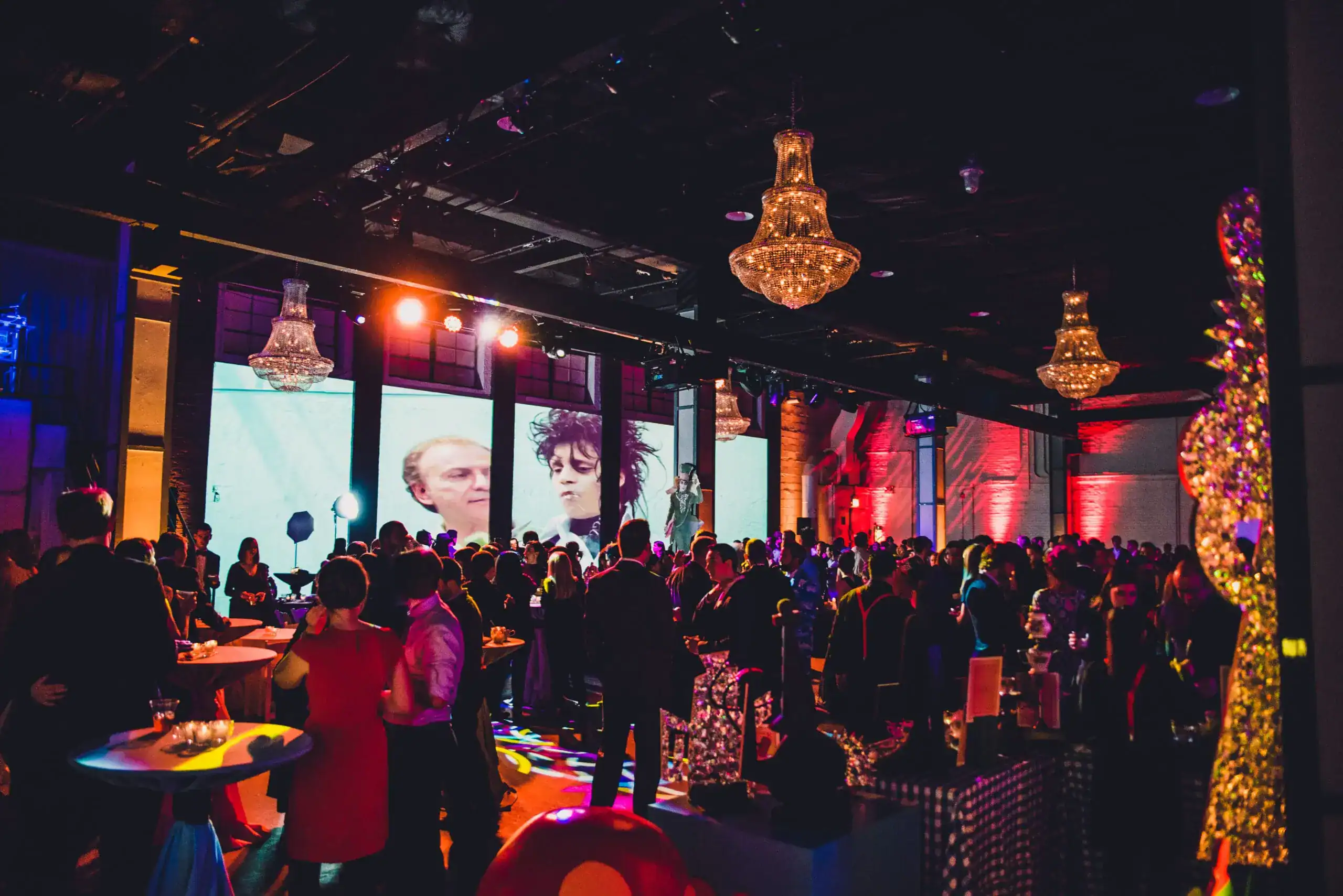 A large group of people socializes at a colorful indoor event with chandeliers, tables, and projected images on the walls, expertly organized by a top Chicago Event Planner.
